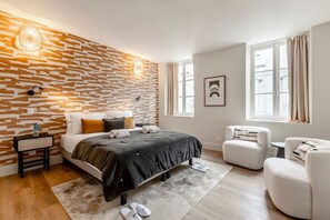 A modern bedroom with a stone-patterned wall, a large bed, a sitting area with a chair, and a window with curtains.