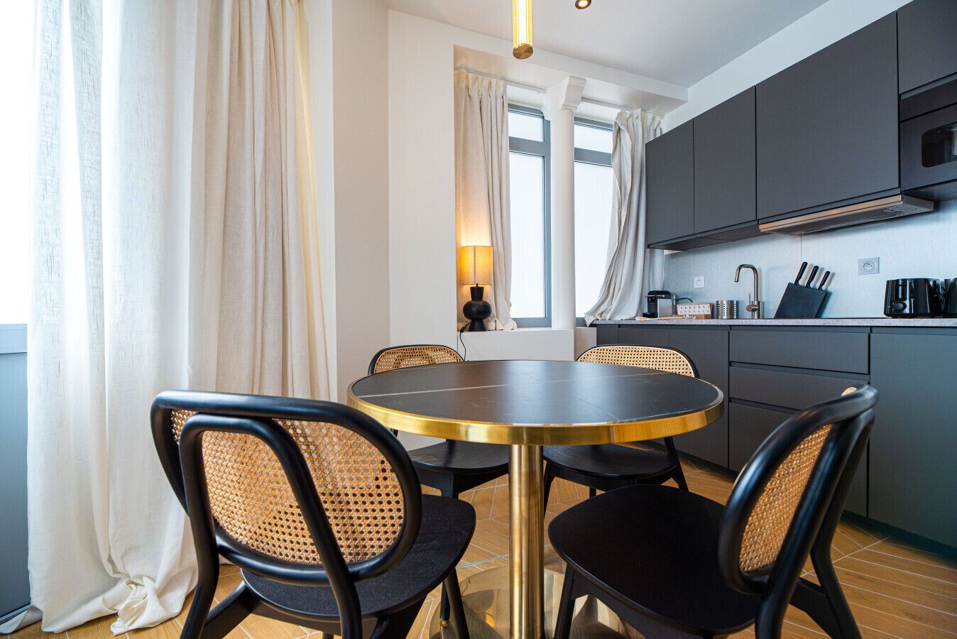 A modern kitchen with dark cabinets, a round table, and four chairs with woven seats.