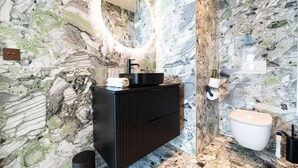 Et badeværelse med marmorvæg, en sort kommode, en vask, et spejl og et toilet.