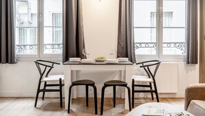 A dining area with a table set for four, two chairs on each side, and a view of the city through large windows. - A1.RépubliqueMarais1BedRoomParis03AC (Paris)