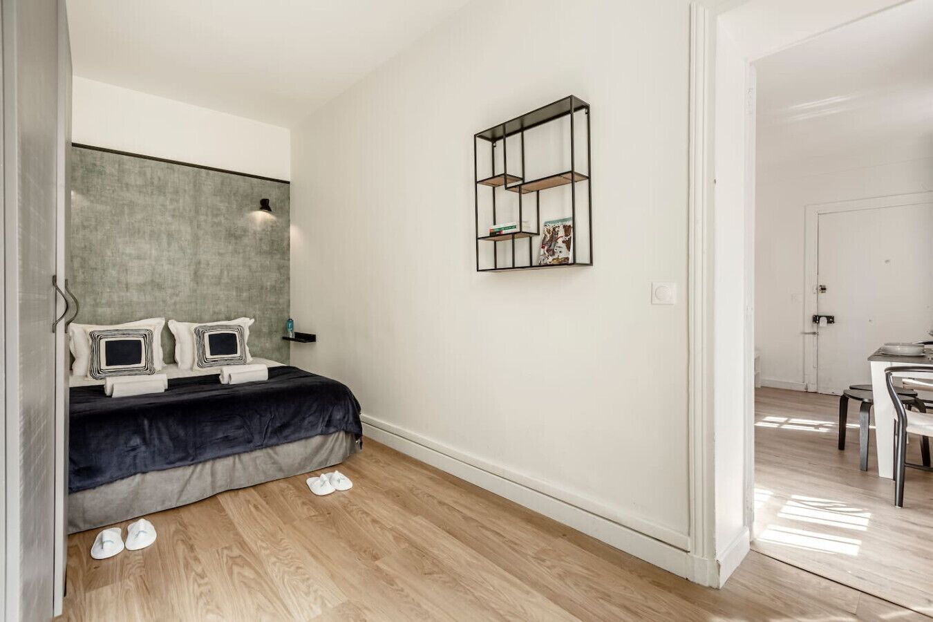 Une chambre à coucher comprenant un lit, des tables de chevet, une étagère fixée au mur et une porte donnant sur une autre pièce.