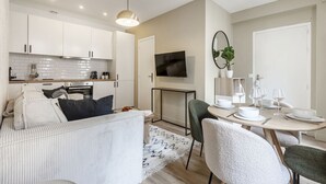 A modern kitchen with white cabinets, a dining area with a round table, and a TV mounted on the wall.