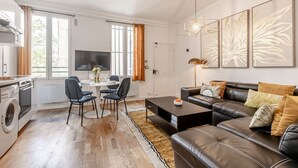 Un salon moderne avec un canapé en cuir noir, une table à manger avec des chaises, un coin cuisine avec un lave-linge et une grande fenêtre avec des rideaux.