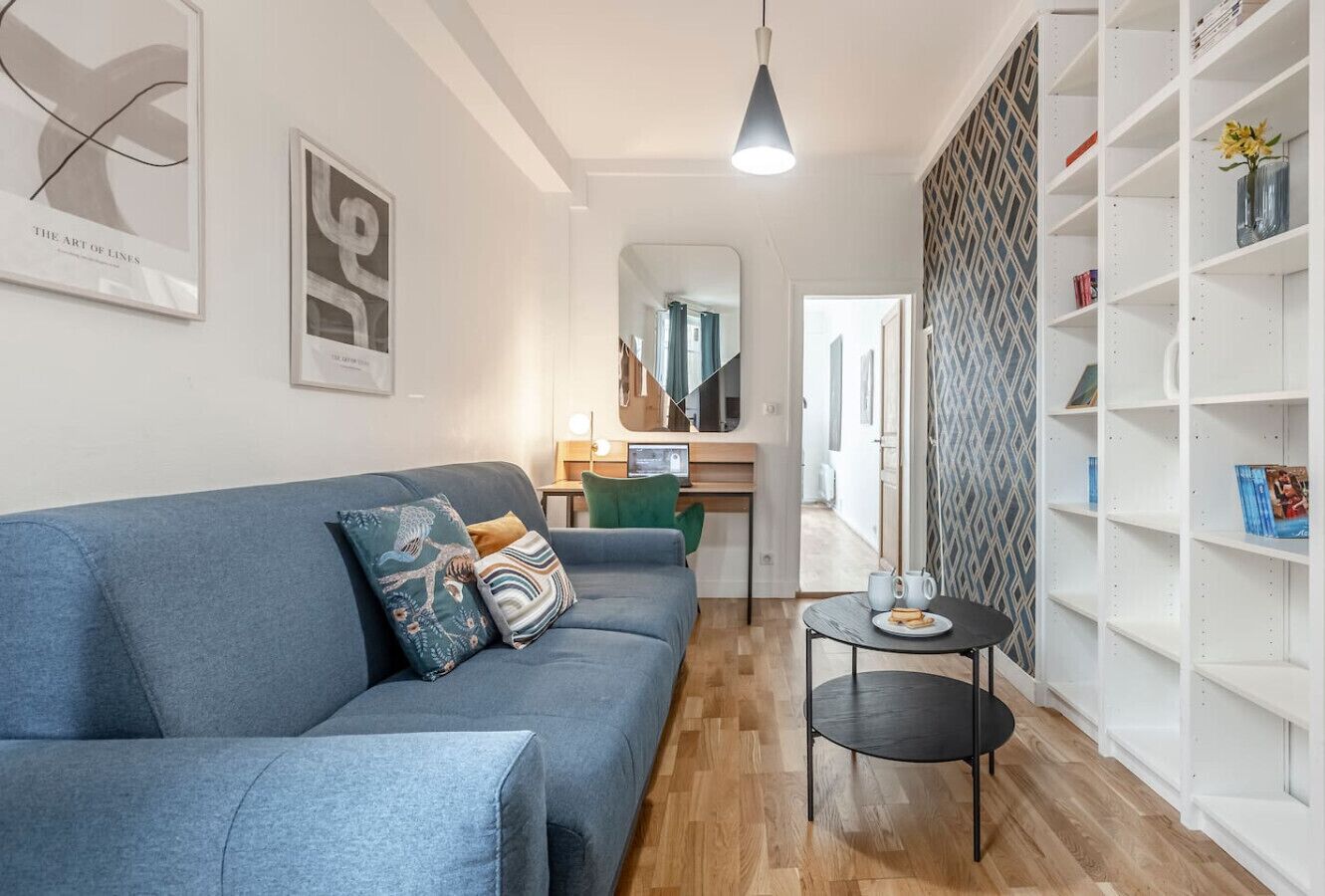 A modern living room with a blue sofa, a small round table, and a white bookshelf.