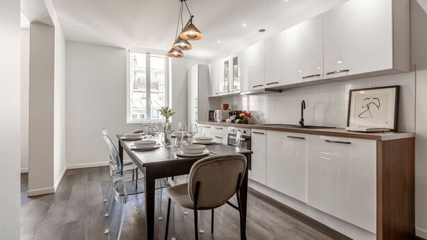 Une cuisine moderne avec des meubles blancs, un plan de travail en bois et un coin repas comprenant une table et des chaises.