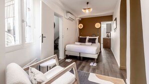 Une chambre moderne avec un lit, des tables de chevet, un petit coin salon et une vue sur le couloir.