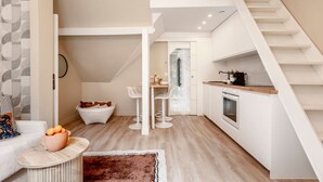 A modern kitchen with white cabinetry, a built-in oven, and a wooden countertop. There is a white dining area with two chairs and a small table. A staircase leads to an upper level. - A41.République#Marais#1BedRoom#Paris03#AC (Paris)