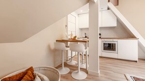 A modern kitchen with white cabinets, a wooden countertop, and a built-in oven. There are three white bar stools and a wicker chair in the foreground. - A41.République#Marais#1BedRoom#Paris03#AC (Paris)