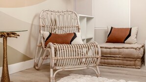 A wicker chair with a cushion, a small table with a glass top, and a sofa with cushions in a room with a white wall and a floor lamp. - A43.République#1BedRoom#Marais#Paris03#AC (Paris)