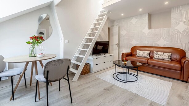 A modern living room with a loft-style staircase, a brown leather sofa, a dining table with chairs, and a decorative vase with flowers. - A43.République#1BedRoom#Marais#Paris03#AC (Paris)