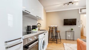 A modern kitchen with a washing machine, a coffee maker, and a TV mounted on the wall.