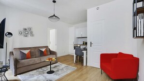A modern living room with a sofa, a red chair, a dining area, and a kitchen.