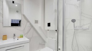 A modern bathroom with a white marble sink, a toilet, and a glass-enclosed shower area.