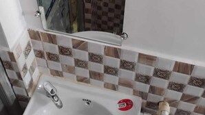A bathroom with a checkered tile backsplash, a mirror, and a sink with a faucet. - Geeta Teerth Guest House (Faizabad)