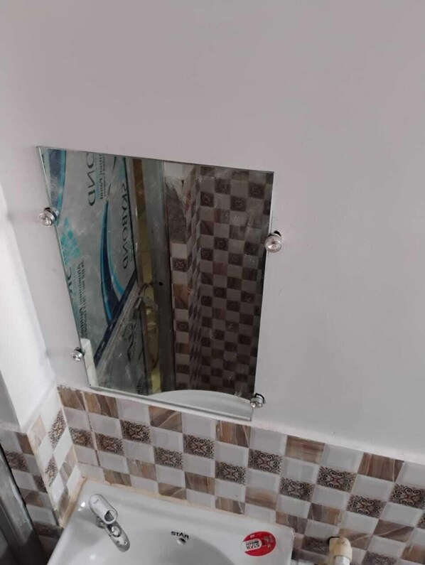 Un baño con salpicadero de azulejos a cuadros, un espejo y un lavabo con grifo.