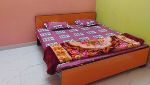A bed with a floral bedspread and two pillows, a wooden headboard, and a green wall to the right. - Geeta Teerth Guest House (Faizabad)