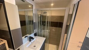 Ein modernes Badezimmer mit einer Duschkabine aus Glas, einem weißen Waschbecken und einem Spiegel.