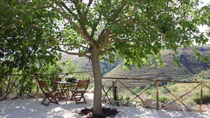 Un arbre sous lequel se trouvent une table et des chaises, le tout entouré d’une zone de gravier offrant une vue sur un paysage vallonné.