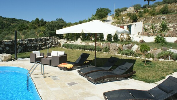 Un espace aménagé au bord de la piscine, avec des chaises longues, un parasol blanc et un mur en pierre.