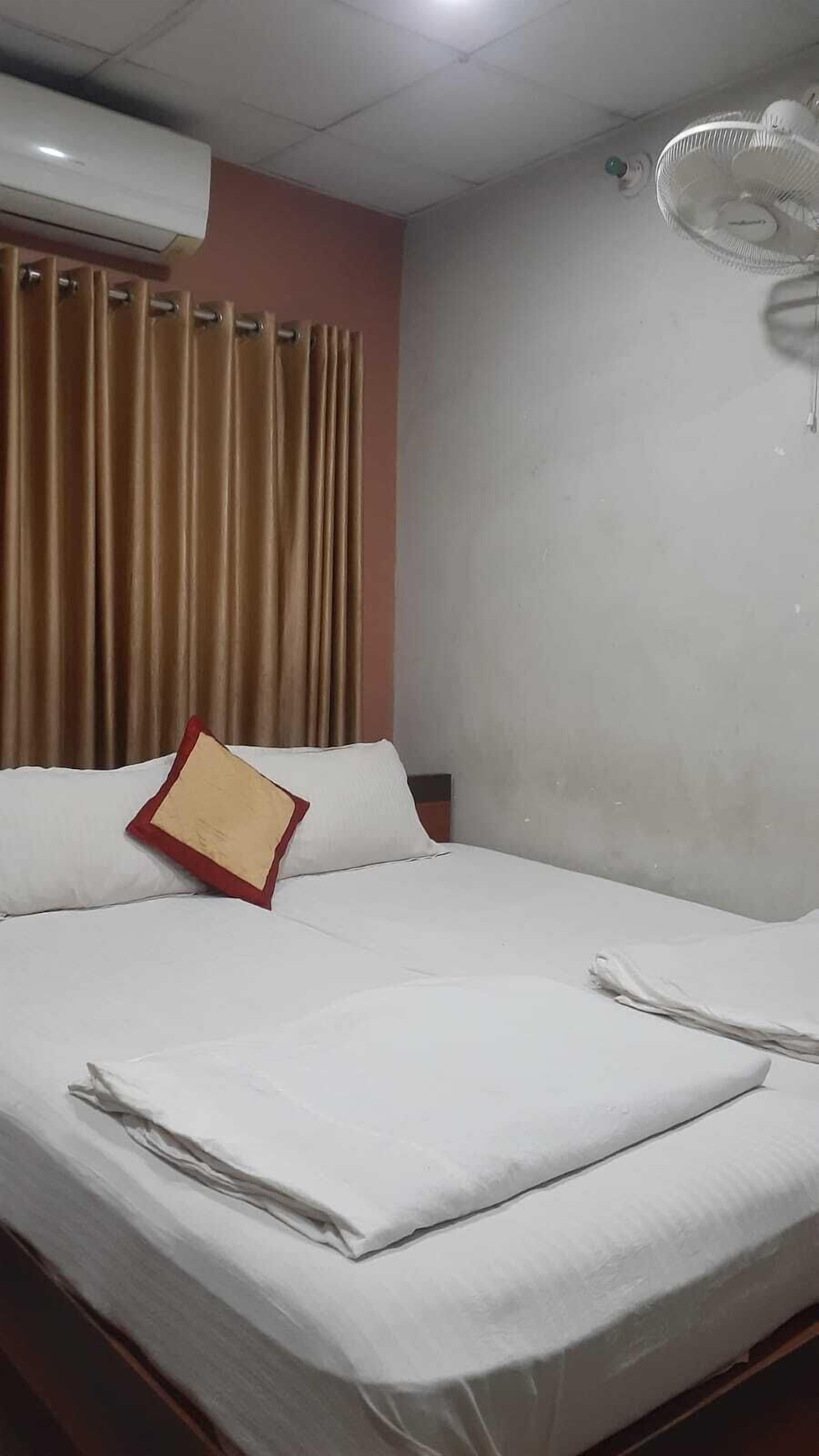 A hotel room with a bed, curtains, an air conditioning unit, and a ceiling fan.