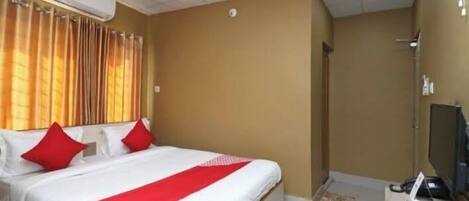 Una habitación de hotel con cama, escritorio, aire acondicionado y zona de ducha.