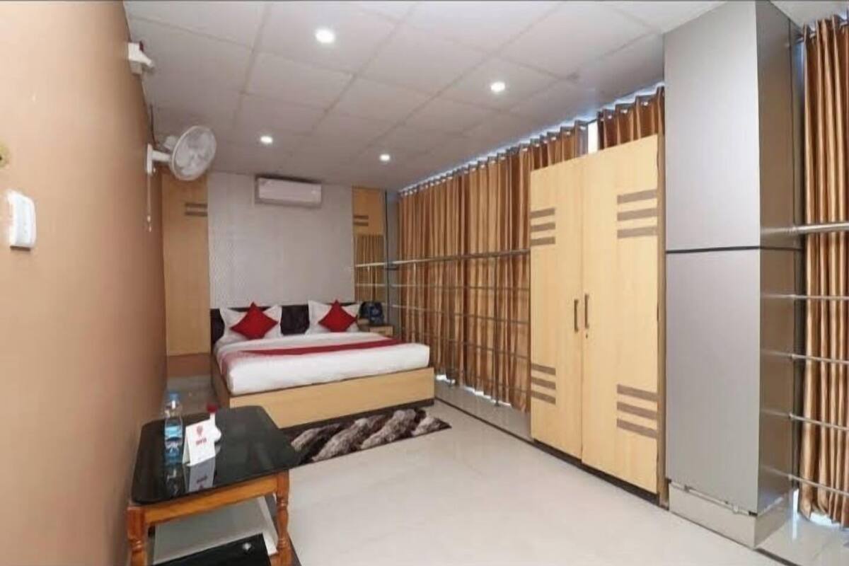 Ett hotellrum med en säng, ett litet bord med en flaska, en fläkt och en garderob med skjutdörrar.