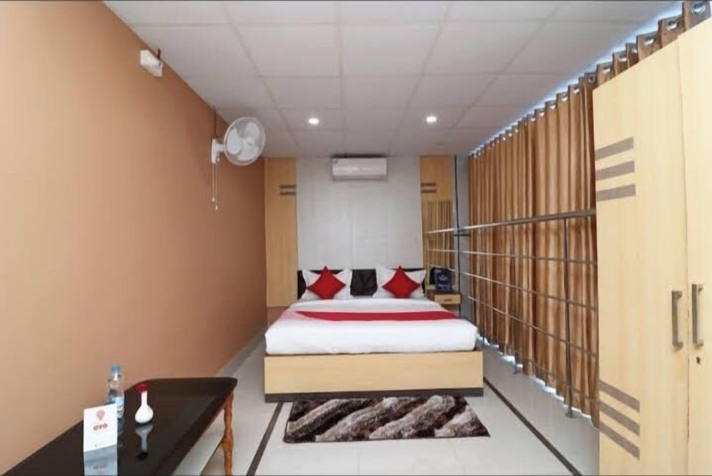 Una habitación de hotel con cama, mesita de noche, ventilador, aire acondicionado y armario.