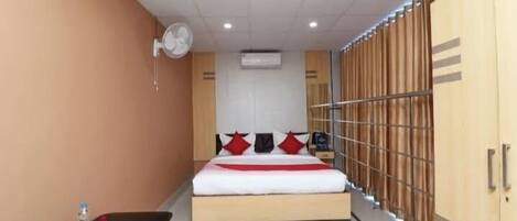 Una habitación de hotel con cama, mesita de noche, ventilador, aire acondicionado y armario.