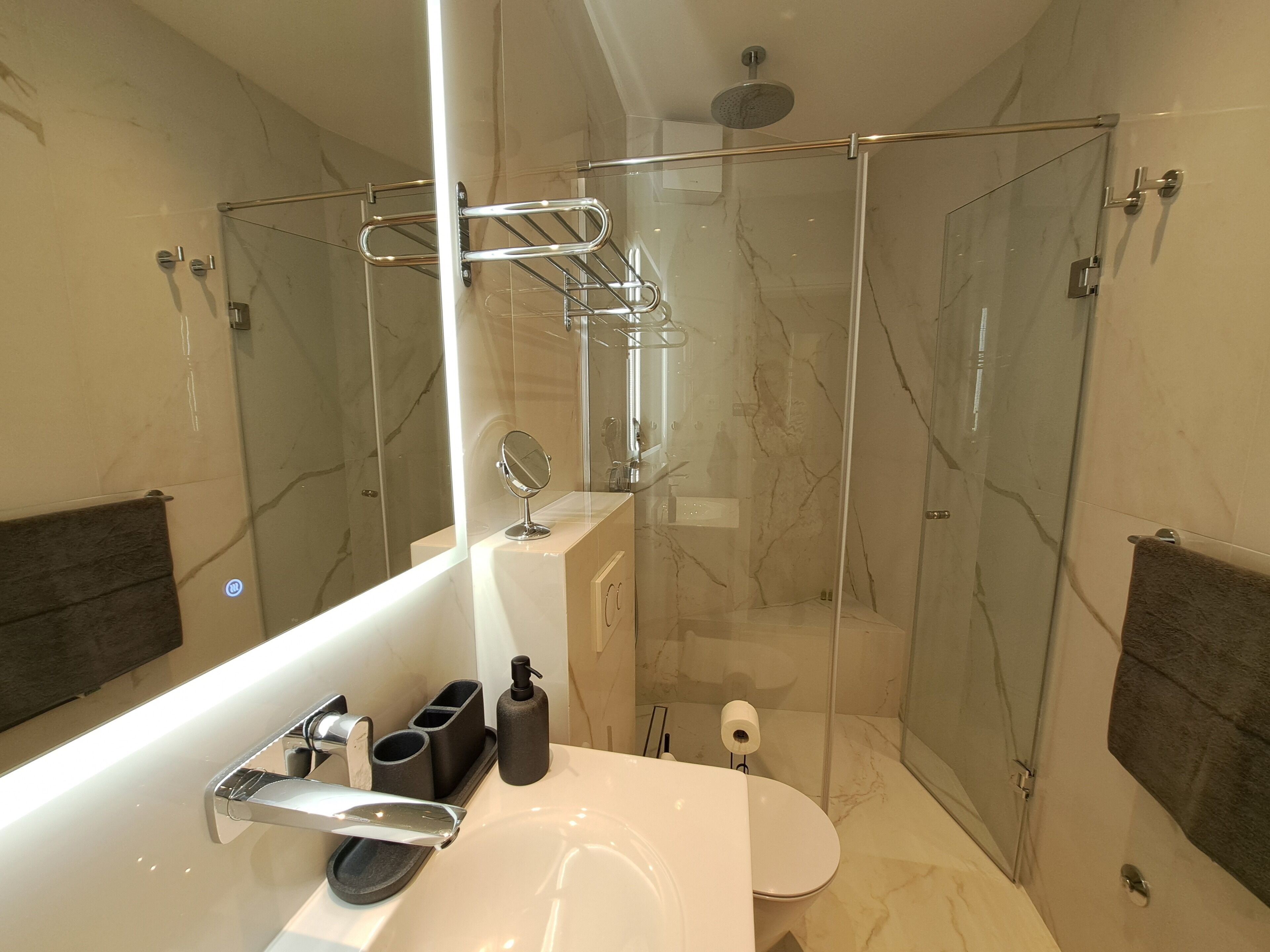 A modern bathroom with a glass-enclosed shower, a large mirror, and a white sink.