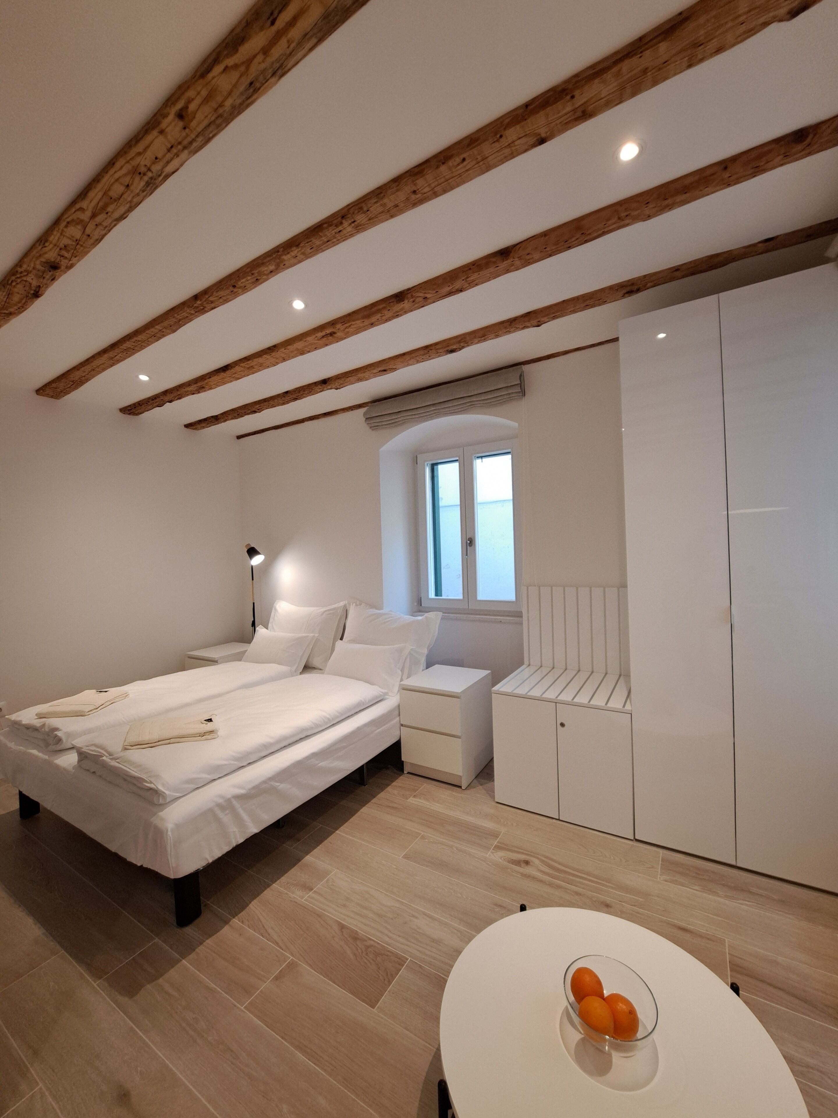 A modern bedroom with a wooden ceiling, a large bed, white furniture, and a small table with fruit.