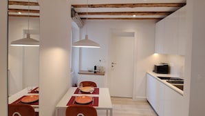 Una cucina moderna con mobili bianchi, soffitto in legno e zona pranzo con tavolo bianco e sedie arancioni.