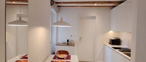 A modern kitchen with white cabinets, a wooden ceiling, and a dining area with a white table and orange chairs.