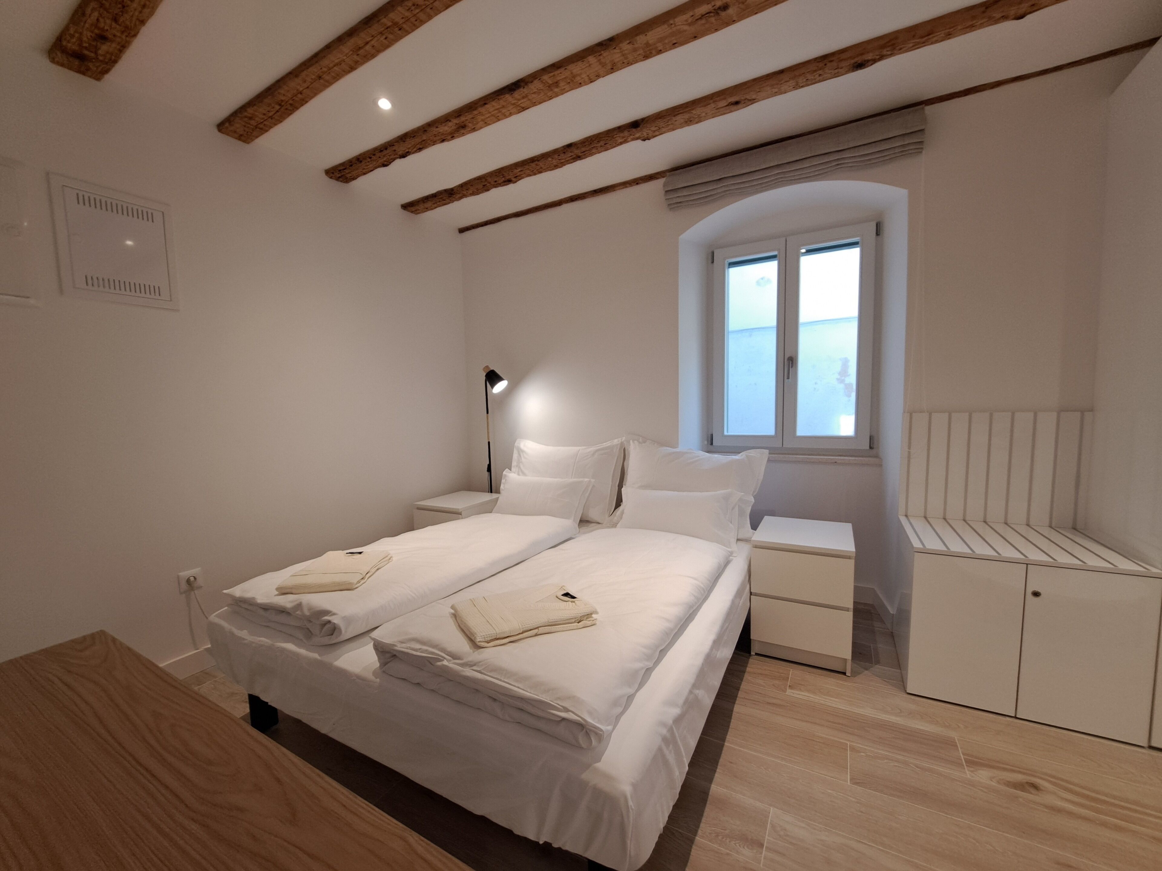 A bedroom with a large bed, bedside tables, a window, and wooden beams on the ceiling.