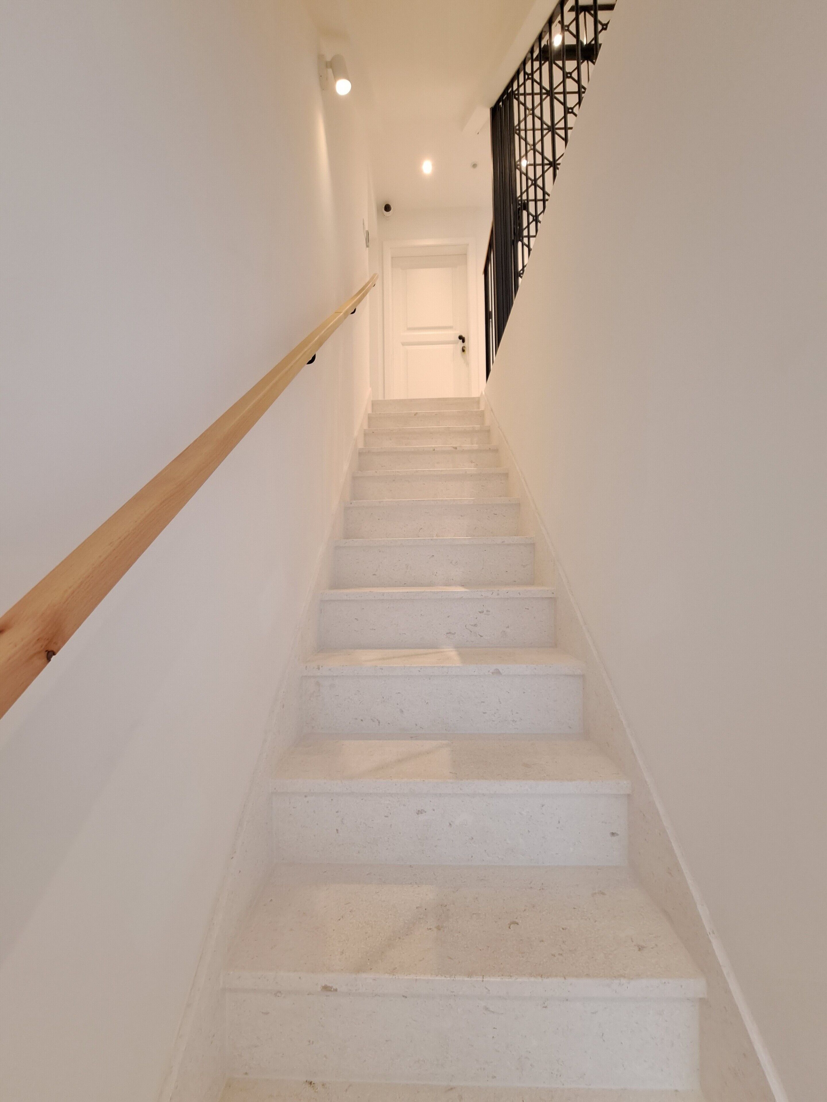 Un escalier avec des marches blanches et une rampe en bois, menant à une porte située en haut.