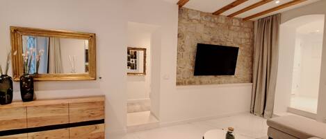 A modern living room with a wooden ceiling, a stone accent wall, a flat-screen TV, a sofa, and a wooden cabinet.