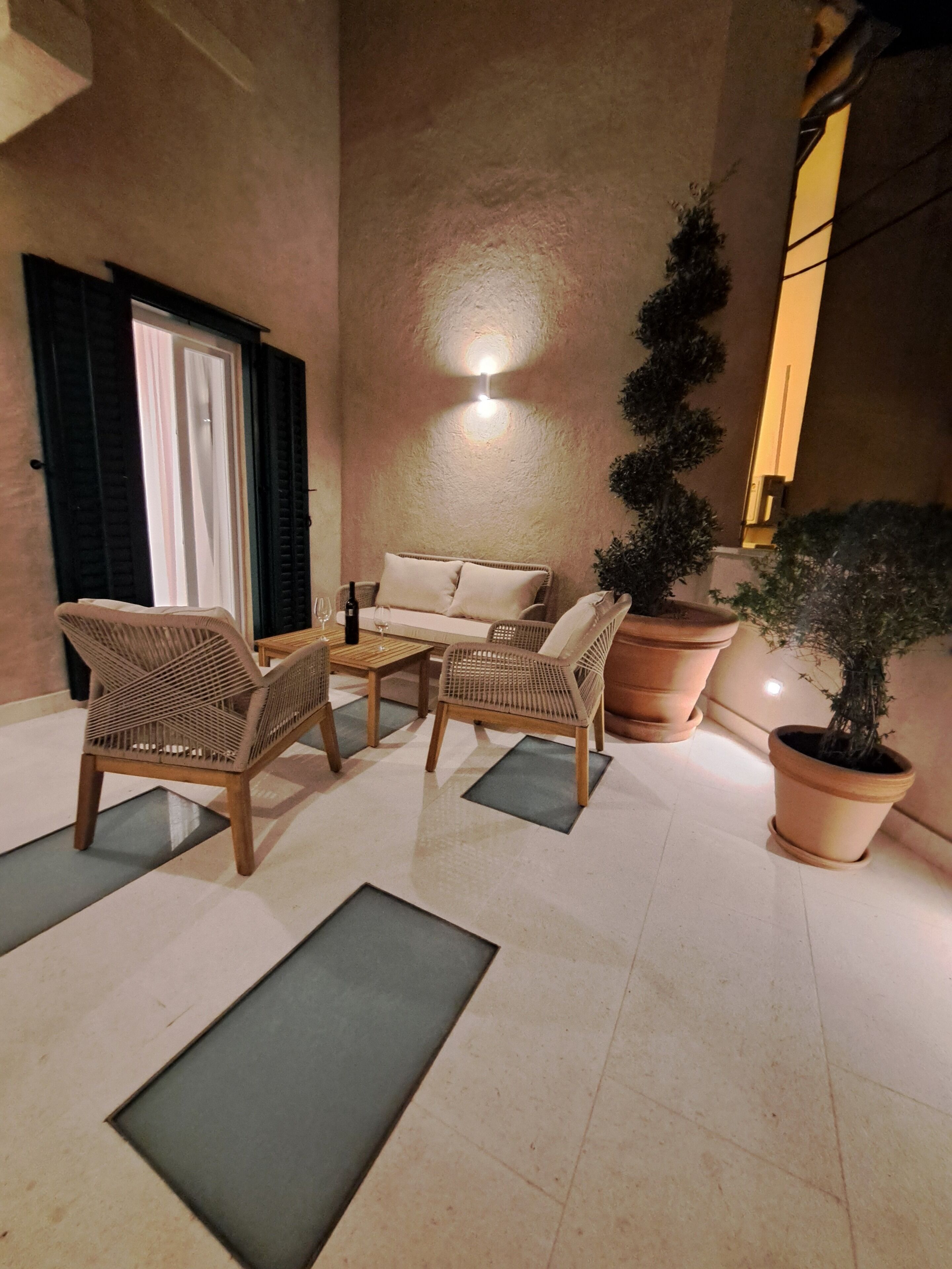 A cozy outdoor seating area with wicker chairs and a sofa, a potted plant, and a wall-mounted light fixture.