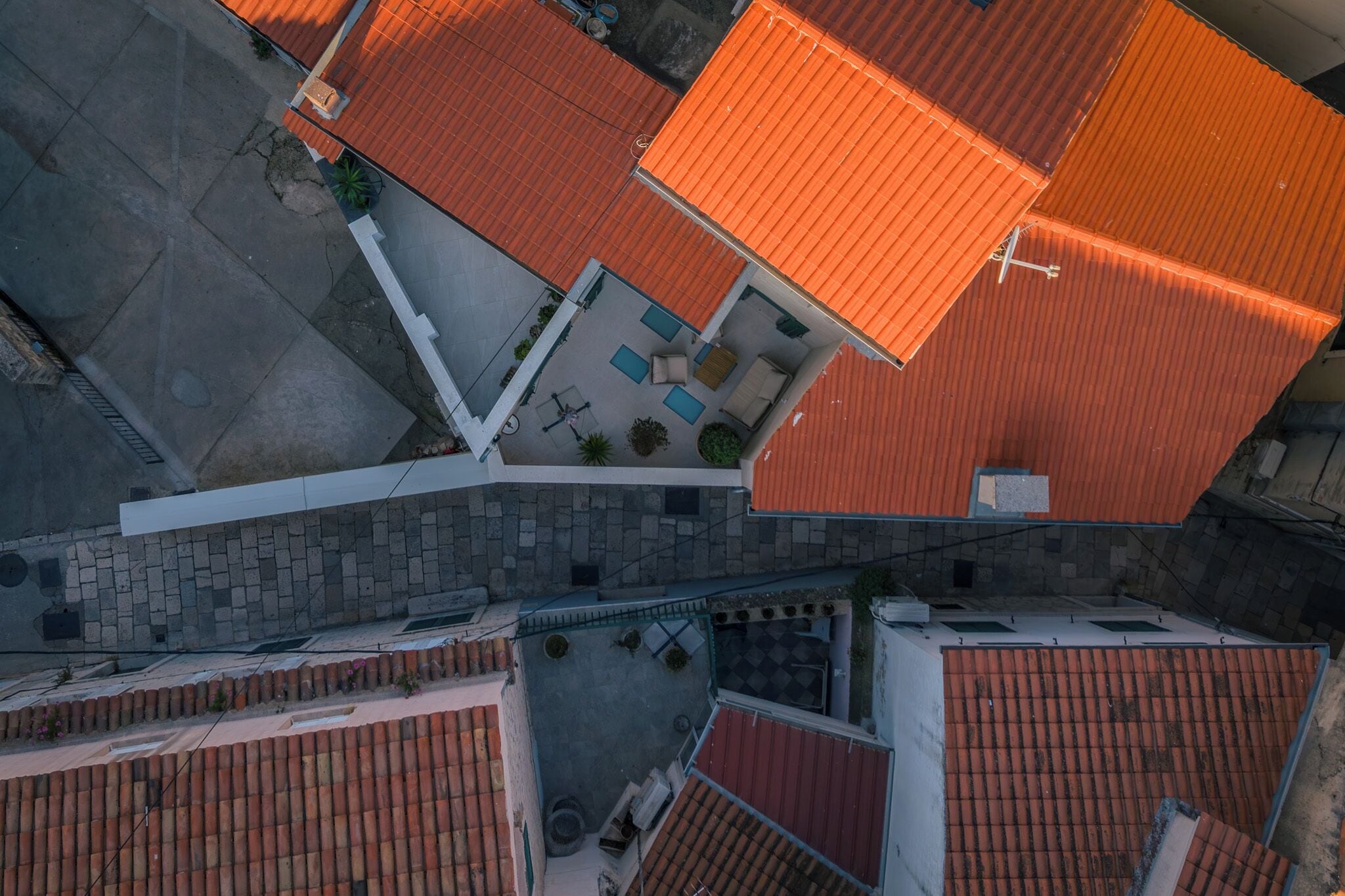 An aerial view of a residential area with red-tiled roofs, a paved courtyard, and a white building with a balcony.