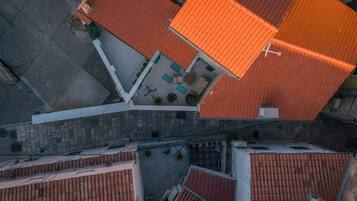 An aerial view of a residential area with red-tiled roofs, a paved courtyard, and a white building with a balcony.