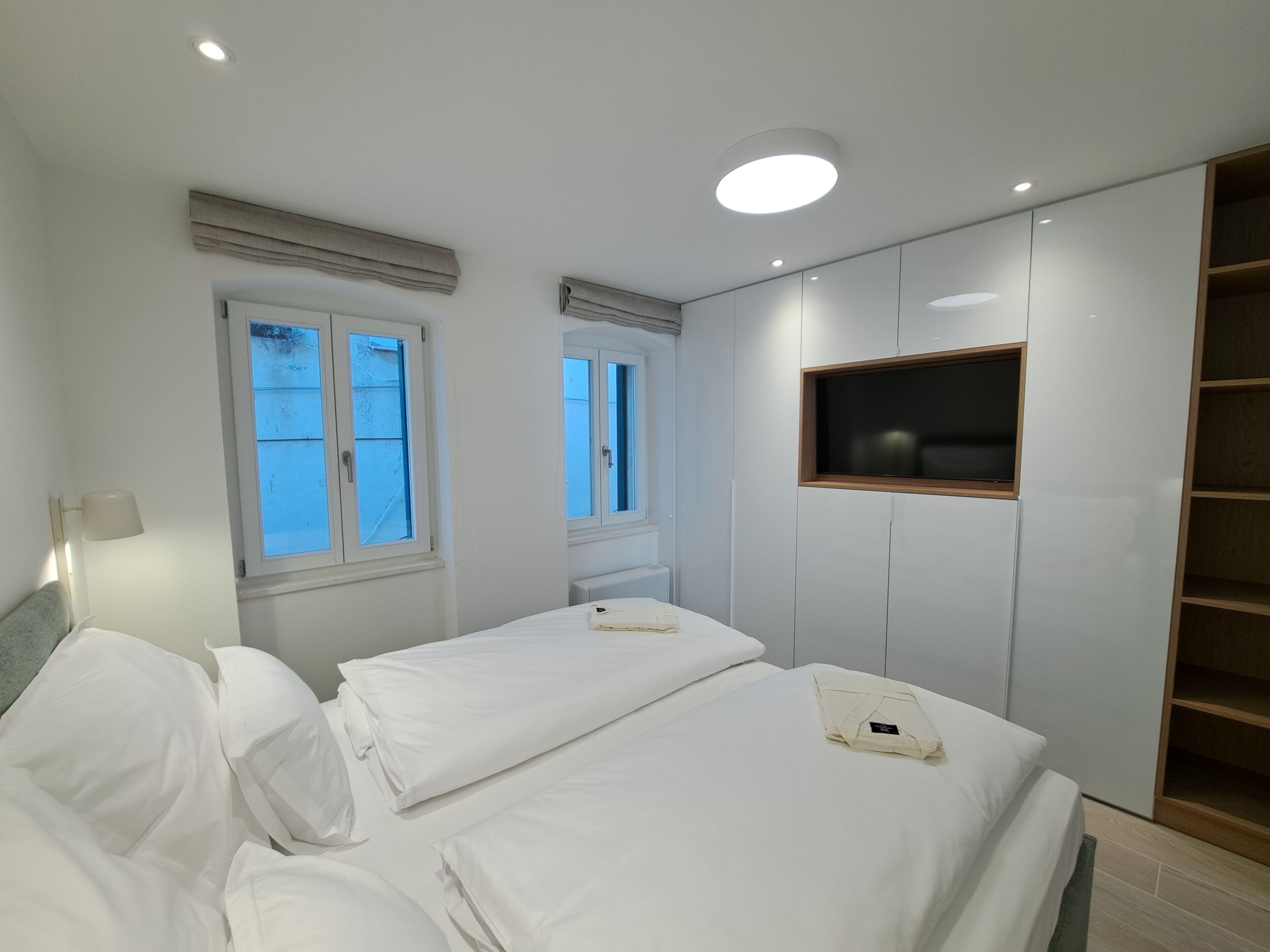 A bedroom with two beds, a window, a TV mounted on the wall, and a lamp.
