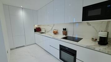 A modern kitchen with white cabinetry, a black microwave, a built-in oven, and a marble countertop.
