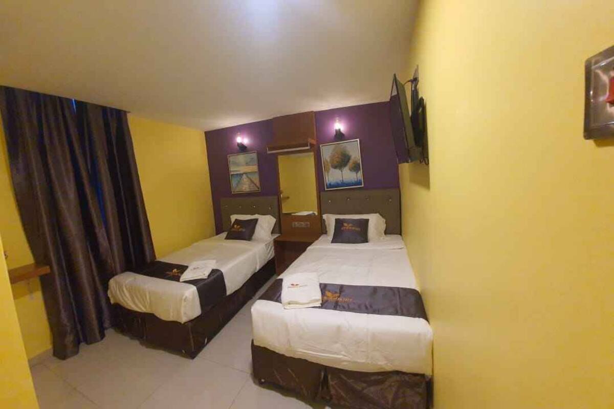 Une chambre d’hôtel avec deux lits, une grande fenêtre avec des rideaux et un téléviseur fixé au mur.