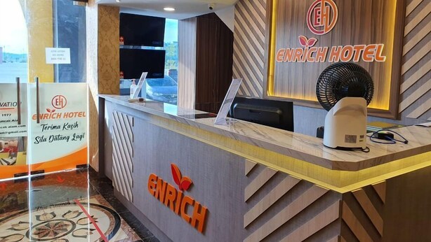 A hotel reception desk with a modern design, including a logo and a sign indicating the hotel's name. - Enrich Hotel Puncak Alam by uBook (Ijok)