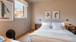 A bedroom with a large bed, a desk, and a window with a view of buildings.