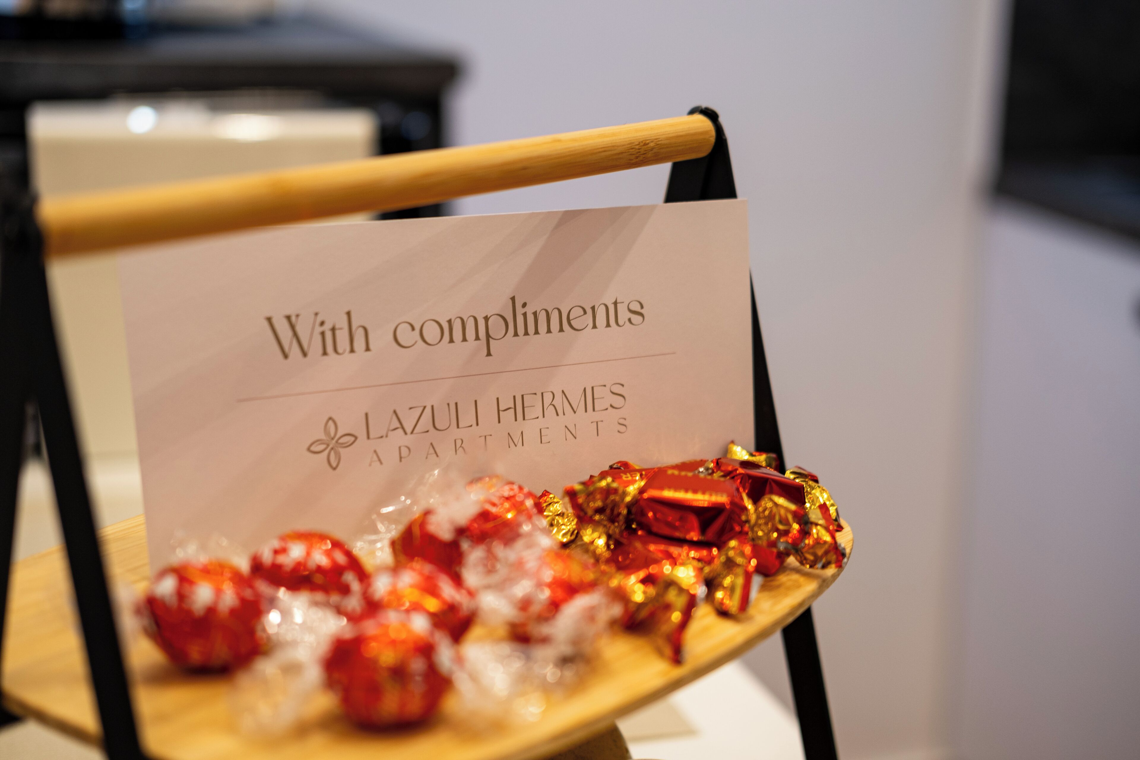 A sign with 'With compliments' and 'LAZULI HERMES APARTMENTS' on a wooden chair.