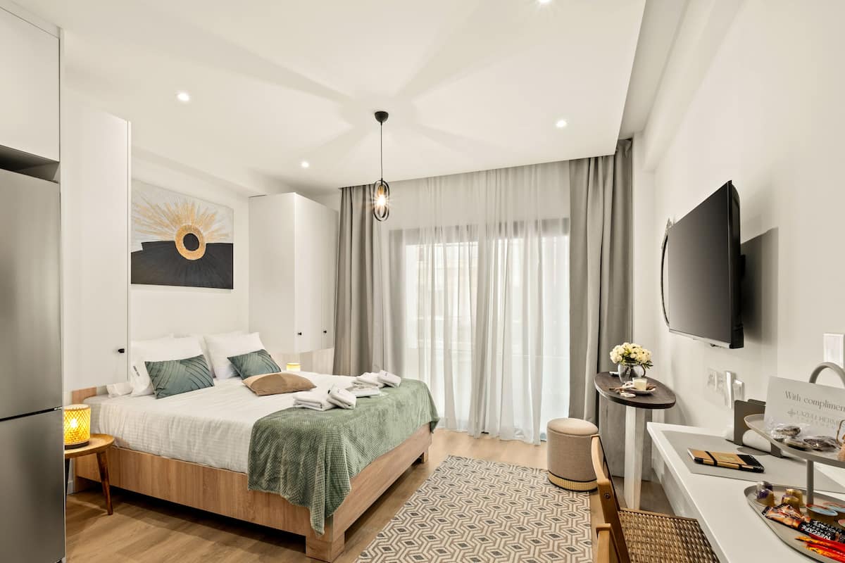 A modern hotel room with a bed, a desk, a TV, and a minibar.