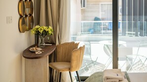 A hotel room with a bed, a chair, a small table with a vase of flowers, and a balcony with a table and chairs. - Lazuli Hermes Apartments (Larnaca)