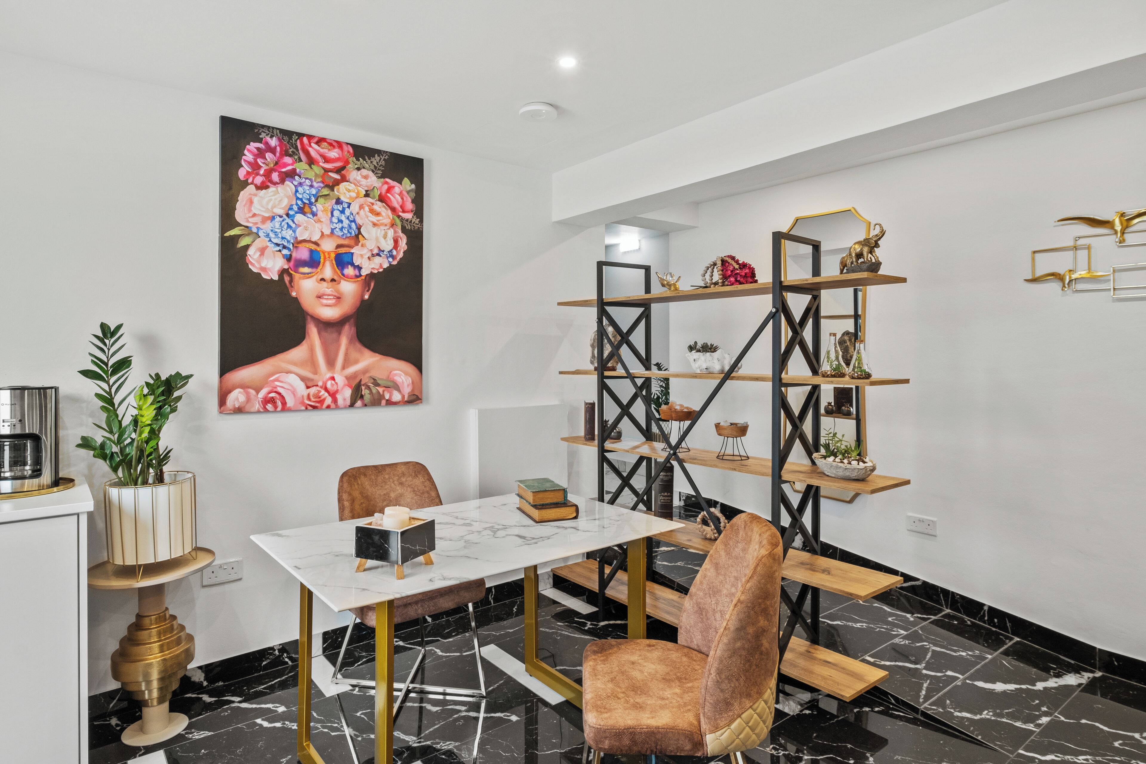 A dining area with a white table, gold accents, and a modern bookshelf with decorative items.