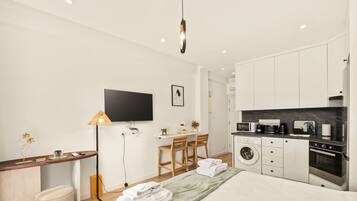 Ein modernes, helles Schlafzimmer mit Bett, Nachttisch, Lampe und einem Flachbildfernseher.