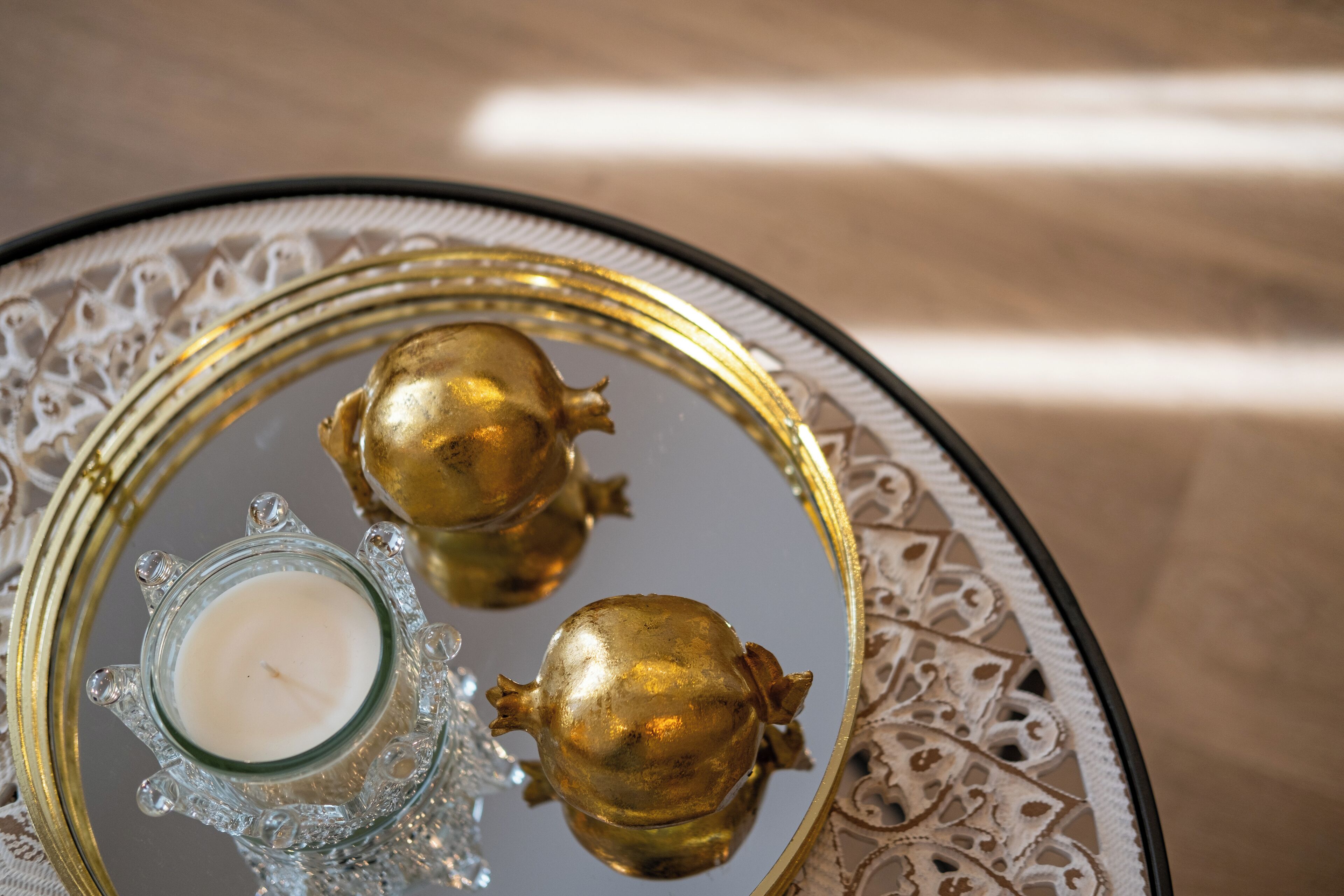 A round table with a glass centerpiece containing a candle and two golden spherical objects.