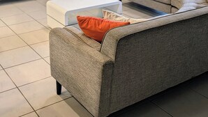 Ein modernes Wohnzimmer mit einem grauen Sofa, einem weißen Couchtisch und einem Flachbildfernseher, der an einer strukturierten Wand angebracht ist.